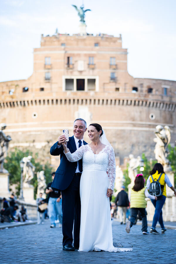 Sposi Novelli couple taking a selfie on Castel S'Angelo Bridge in Rome