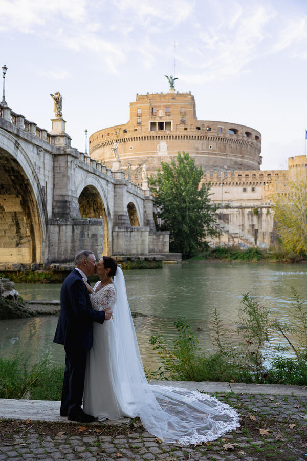 Sposi Novelli couple kissing on the Tiber riverbank and Castel Sant'Angelo in the background