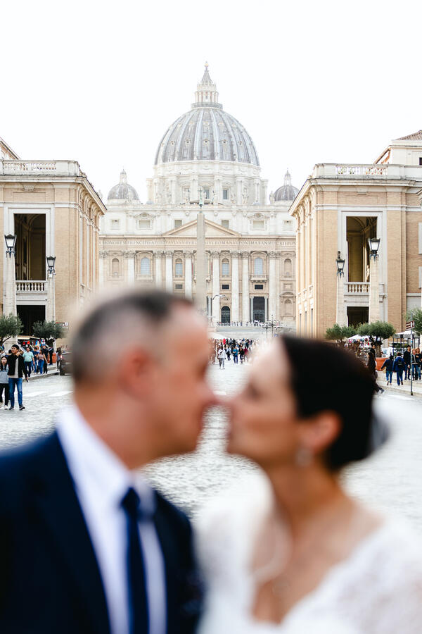 Newly-wed couple out of focus in the foreground with the Vatican in focus in the background