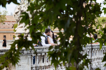 A view of a wedding couple kissing through the foliage on Umberto Bridge, in Rome