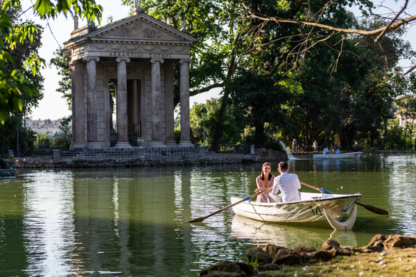 Honeymoon couple on a rowboat at the lake in the Villa Borghese, with the Temple of Esculapio in the background.