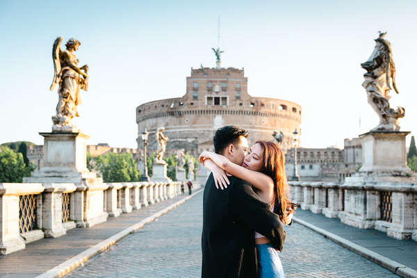 Newly-engaged couple embracing in Rome on Castel Sant'Angelo Bridge during their Surprise Proposal Photoshoot