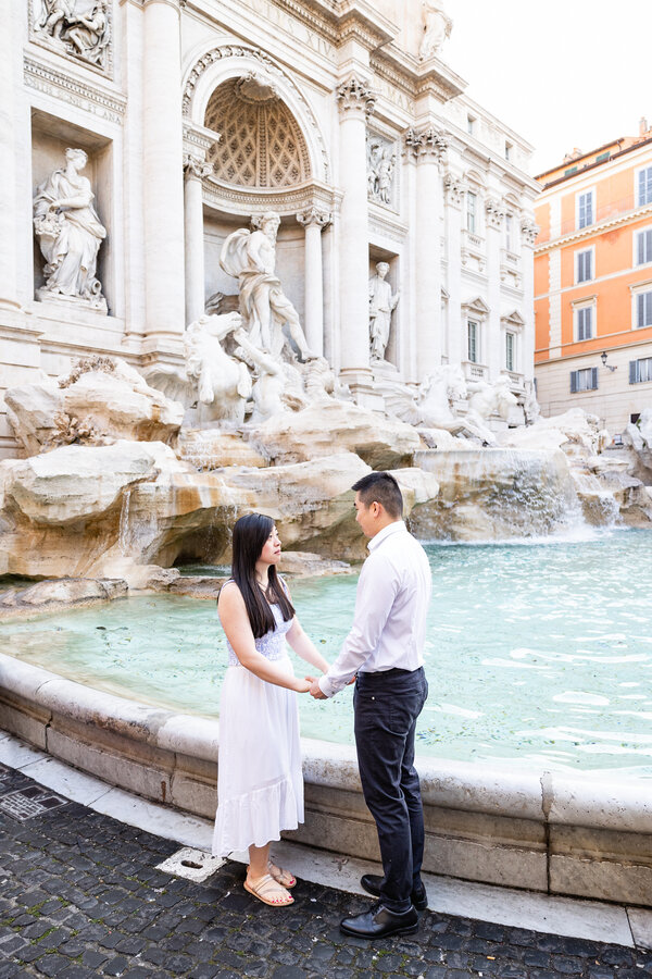 Couple holding hands during their Surprise marriage proposal photoshoot at the Trevi Fountain in Rome in the early morning