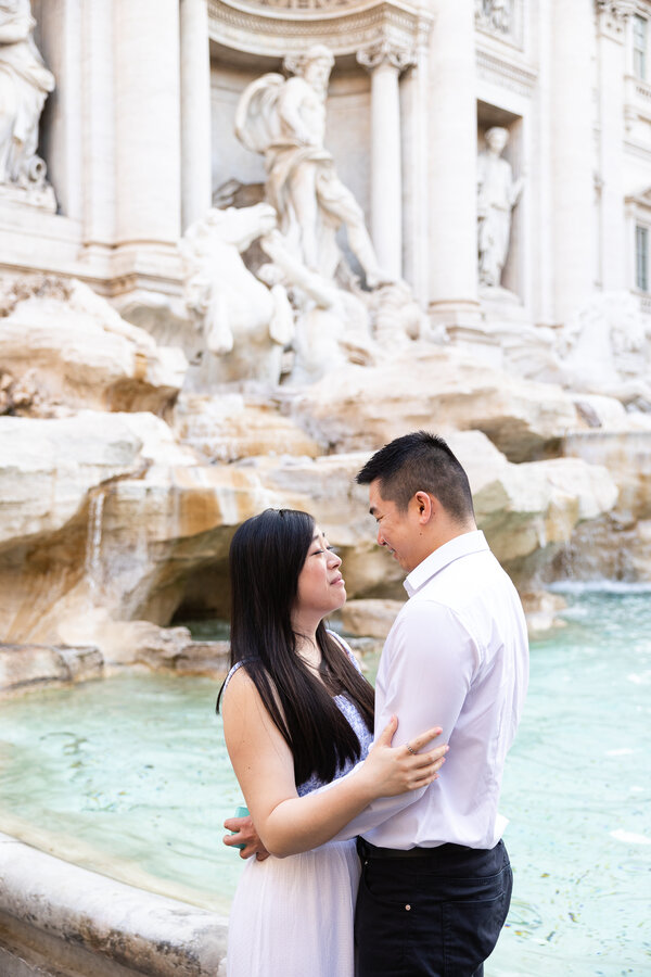 Newly-engaged couple holding and looking at each other at the Trevi Fountain