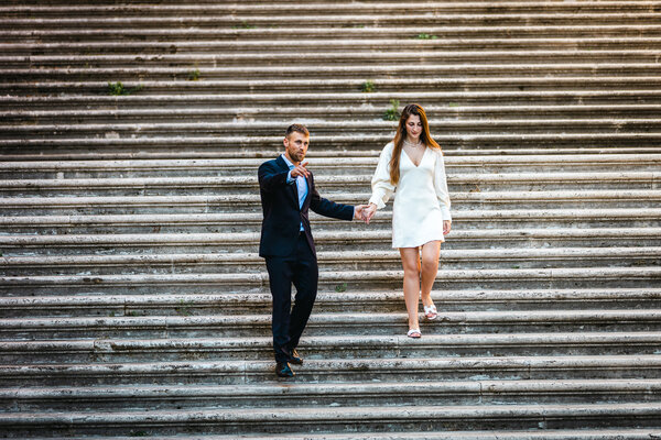 Beautiful elegant couple coming downt the staircase at the Capitoline Hill during their engagement photo shoot in Rome