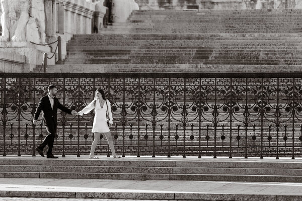 Black and white image of newly-engaged couple walking along the Vittoriano steps in Piazza Venezia in Rome