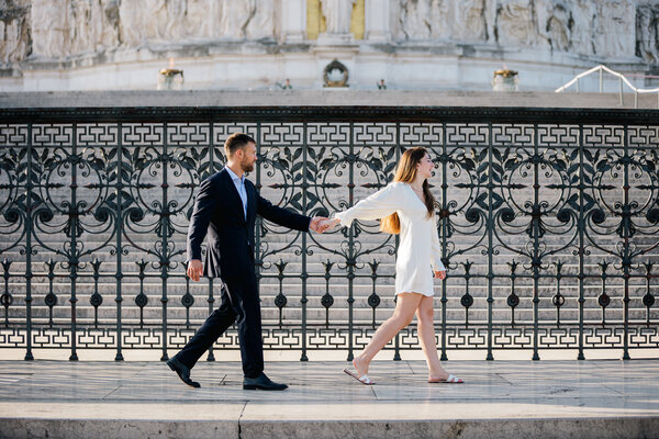 Newly-engaged couple holding hands and walking along the steps on the Vittoriano in Piazza Venezia in Rome