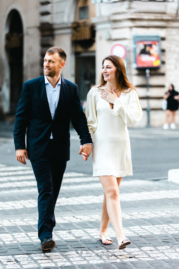 Newly-engaged couple holding hands, crossing the road on the zebra crossing during their engagement photo session in Rome