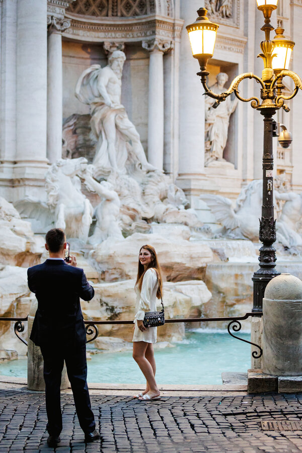 Man in suit taking a picture of his girlfriend at the Trevi Fountain at sunrise