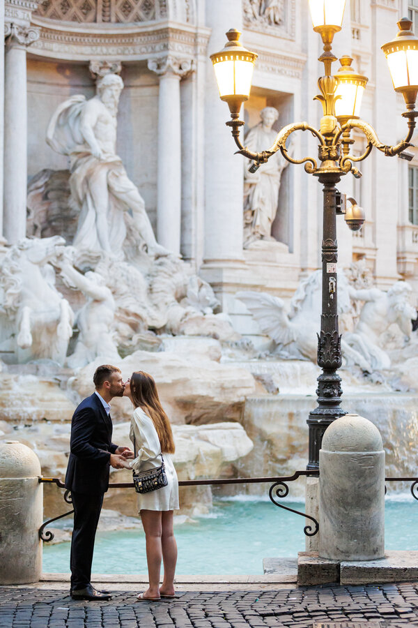 Elegant couple kissing at the Trevi Fountain at sunrise