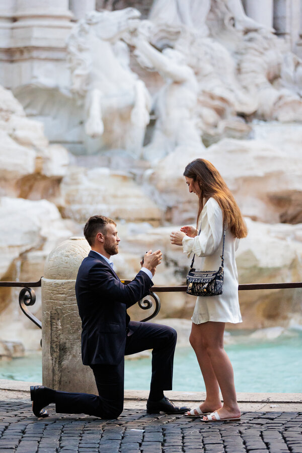 Fiancé on his knee opening the ring box to deliver the ring to his fiancée at the Trevi Fountain in Rome