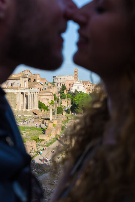 Couple about to kiss in a blurred foreground with the Forum and the Colosseam in focus in the background