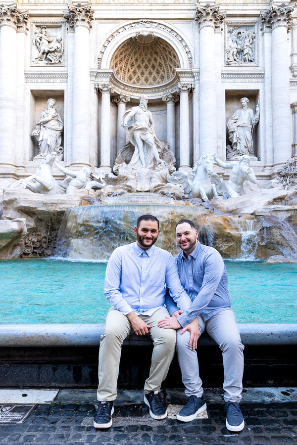 Happy newly-engaged couple sitting by the water at the Trevi Fountain in Rome