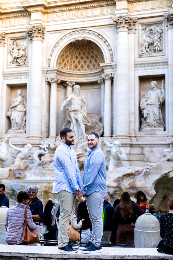Newly-engaged happy couple holding hands during their same-sex surprise proposal photoshoot by the Trevi Fountain in Rome