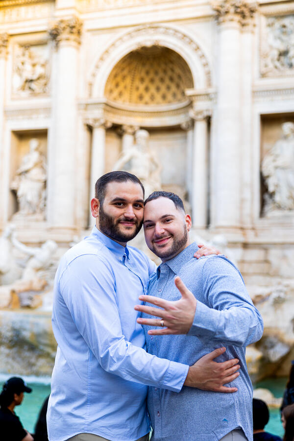Newly-engaged happy couple holding each other during their same-sex surprise proposal photoshoot by the Trevi Fountain in Rome