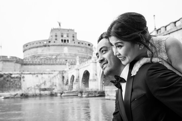 Black and white image of newly-wed couple during a Sposi Novelli photo shoot, with Castel Sant'Angelo in the background, Rome