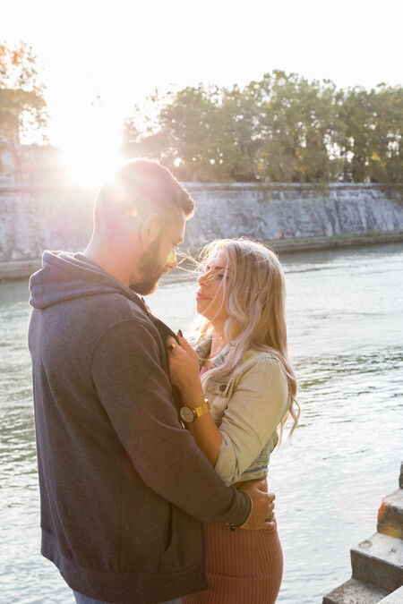 A couple looking at each other on the Tiber riverbank at sunset in Rome
