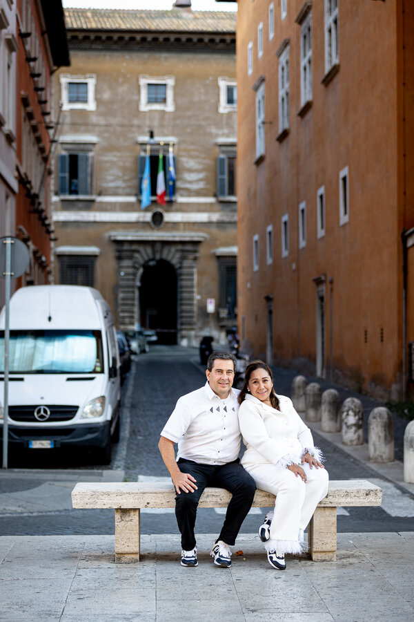 Couple sitting on a bench along Via della Conciliazione during their wedding anniversary photo shoot in Rome