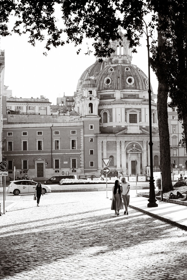 Black and white image of newly-engaged couple walking in Piazza Venezia in Rome