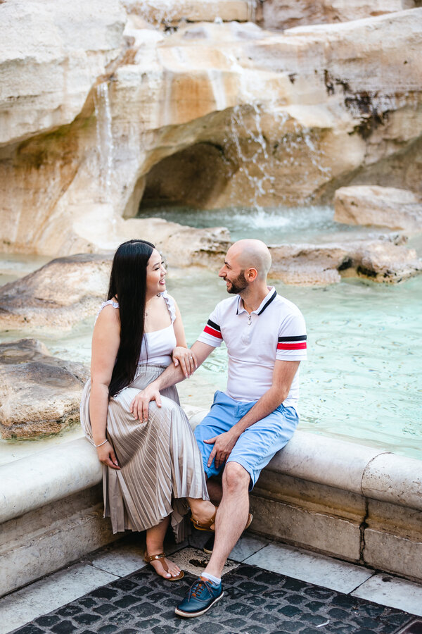 Happy newly-engaged couple sitting on the rim of the Trevi Fountain during their Engagement Photoshoot