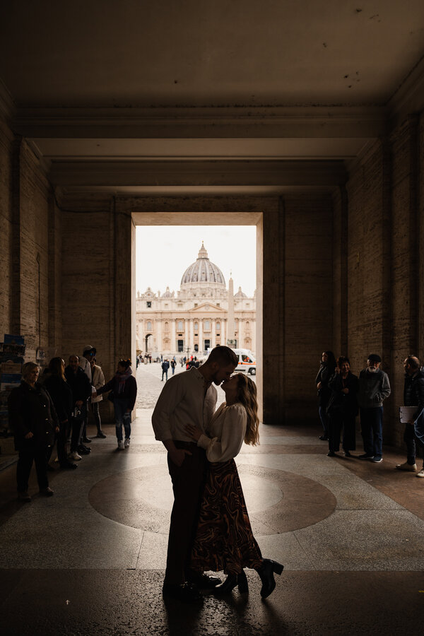 Newly-engaged couple sweetly kissing with bystanders looking on near Saint Peter's Square in Rome