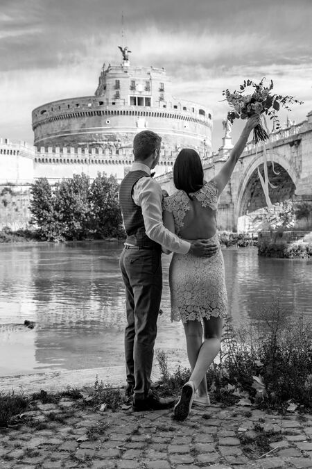 A black and white image of a young newly-weds looking at Castel Sant'Angelo during their destination wedding photo session