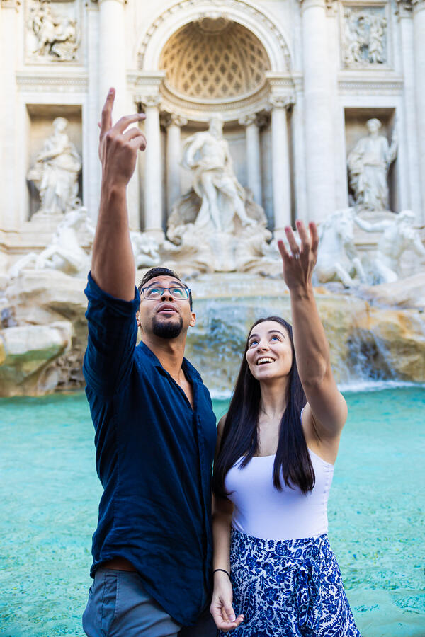 Newly-engaged couple making a wish to come back to Rome while throwing a coin into the Trevi Fountain