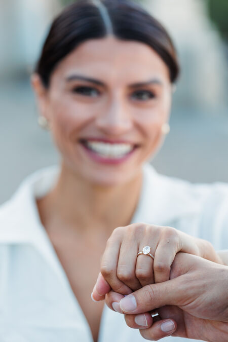 Beautiful woman smiling in the background with her hand wearing the engagement ring in the foreground