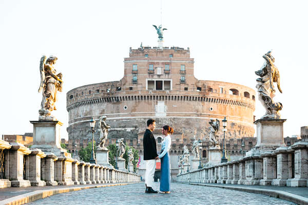 Young couple standing in the middle of Castel Sant'Angelo Bridge moments before their marriage proposal in Rome