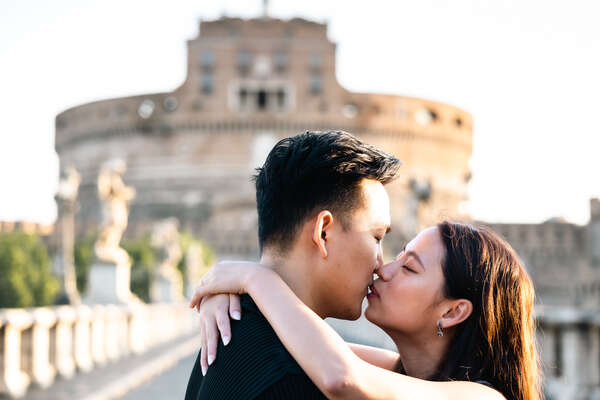 Newly-engaged couple kissing with Castel Sant'Angelo in the background during their surprise proposal photo session in Rome