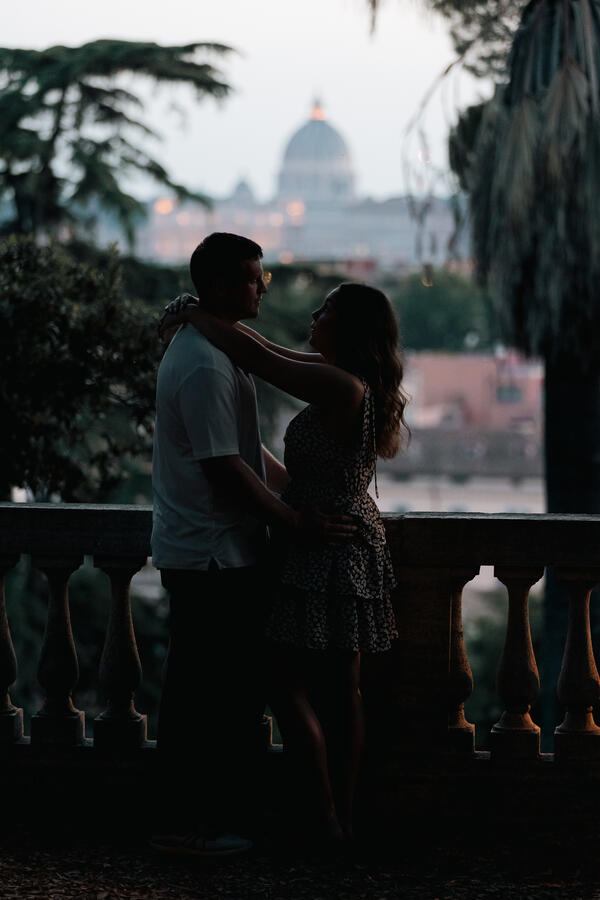 Newly-engaged couple holding each other at under the trees at the Pincio Gardens with the Colosseum in the background