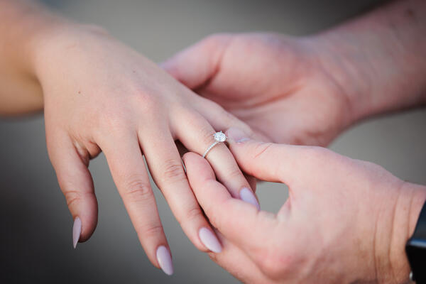 Detail of fiance putting on the engagemnt ring on his finacée