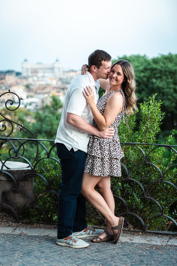 Newly-engaged couple posing while on their surprise proposal photo session on the Terrazza Belvedere at sunset in Rome