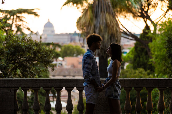 Newly-engaged couple holding each other with the Vatican in the background at sunset on the Pincian Hill in Rome