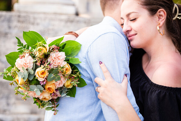 Newly-engaged couple in each other's arms while holding their proposal bouquet at the Pincio Gardens in Rome