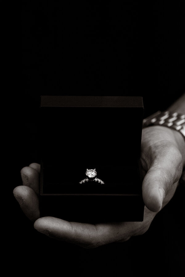 Black and white image of engagement ring in ringbox held by hand
