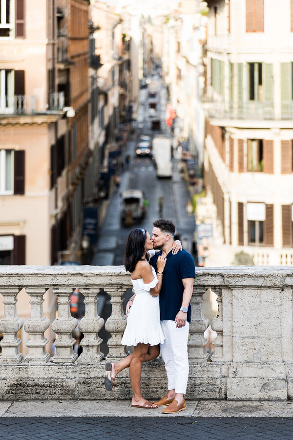Newly-engaged couple kissing on the Spanish Steps with Via Condotti in the background