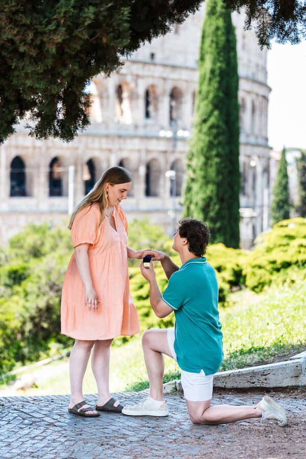 Guy in on his knee opening the engagement ring box during a surprise marriage proposal in Rome with the Colosseum in the background