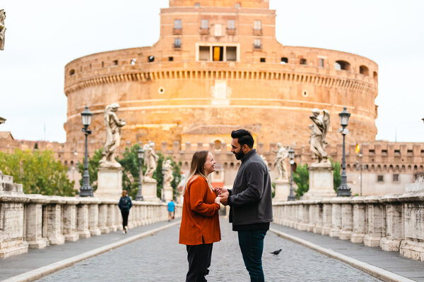 Couple holding hands on Castel Sant'Angelo Bridge at sunrise, moments before their wedding proposal in Rome