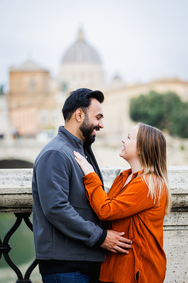 Happy newly-engaged couple holding and smiling at each other with the Vatican in the background