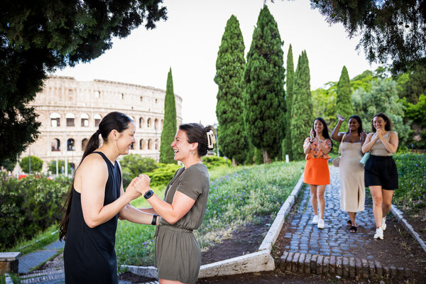 Newly-engaged couple during their surprise proposal photoshoot near the Colosseum in Rome with friends showing up 