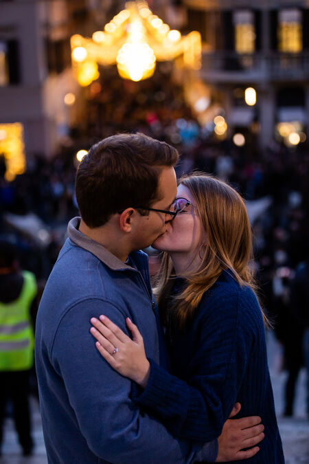 Couple kissing each other on the Spanish at night with Christmas lights in the background