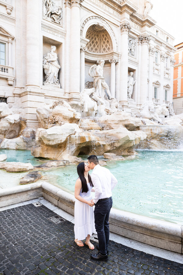 Newly-engaged couple kissing after their surprise proposal at the Trevi Fountain