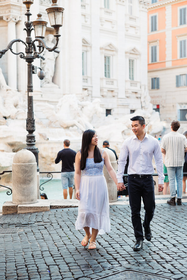 Newly-engaged couple walking at the Trevi Fountain during their surprise proposal photoshoot in Rome