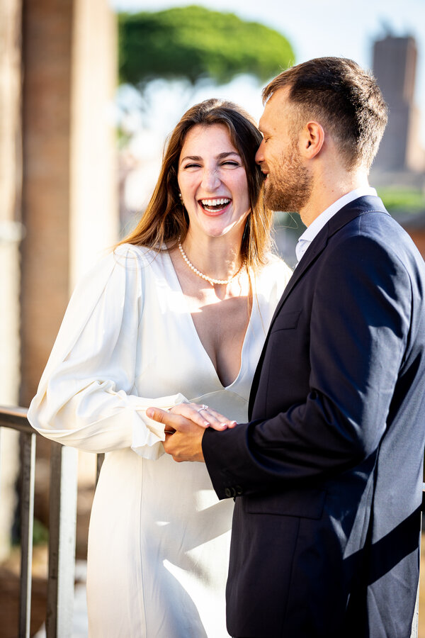 Newly-engaged fiancé whispering in his fiancée's ears and making her smile during their engagement photo shoot on the Capitoline Hill in Rome