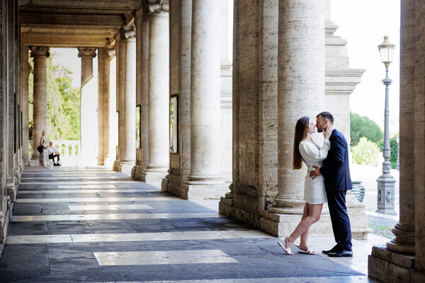 Newly-engaged kissing under the colonnade on the Capitoline HIll during their engagement photo session in Rome