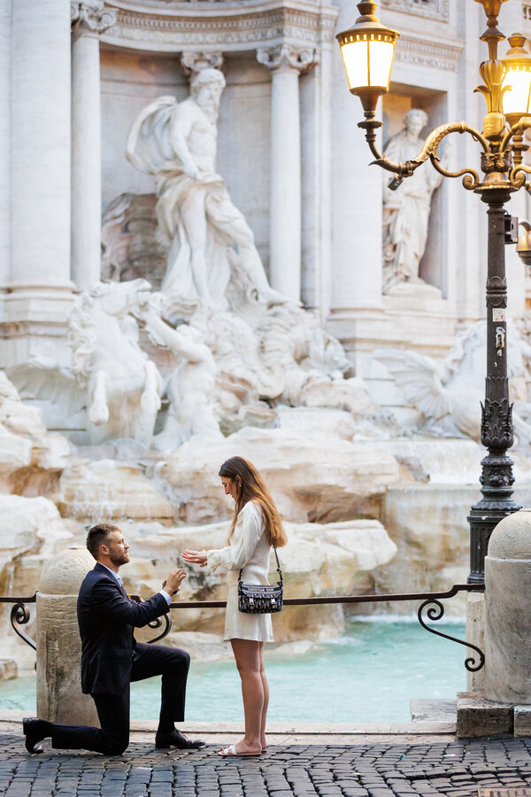 Fiancé on his knee putting the ring on his fiancée at the Trevi Fountain in Rome