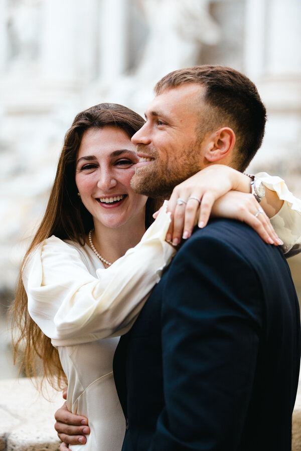 Newly-engaged couple smiling at the Trevi Fountain early in the morning