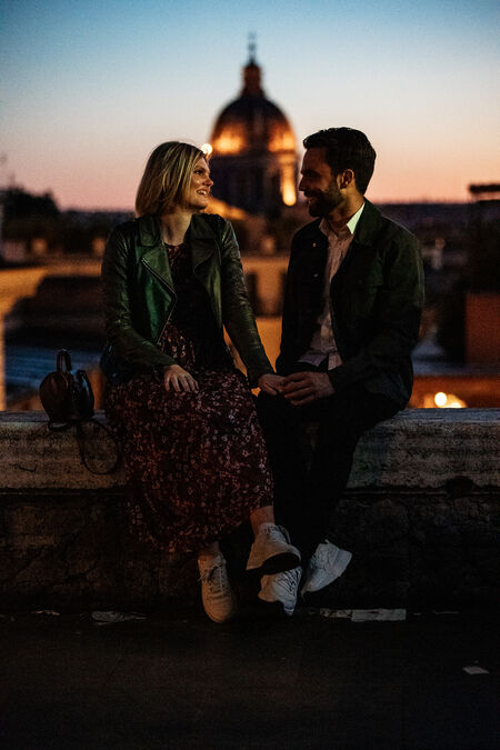 Happy couple sitting in the golden hour and holding each other's hands with Rome as a beautiful backdrop