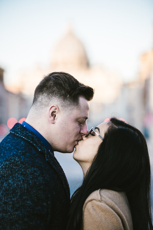 Newly-engaged couple kissing passionately with the Vatican out of focus in the background
